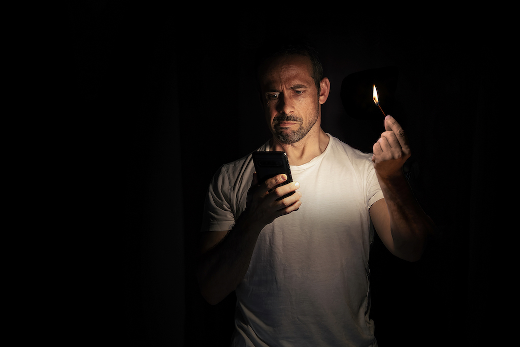 Man holding match and looking at phone hoping for emergency generator services.