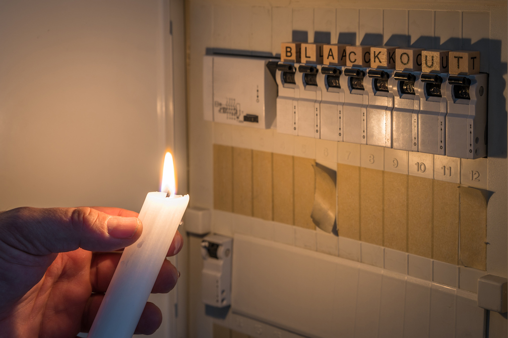 Person holding a candle to switch board with the world blackout, in need of emergency electrical services.