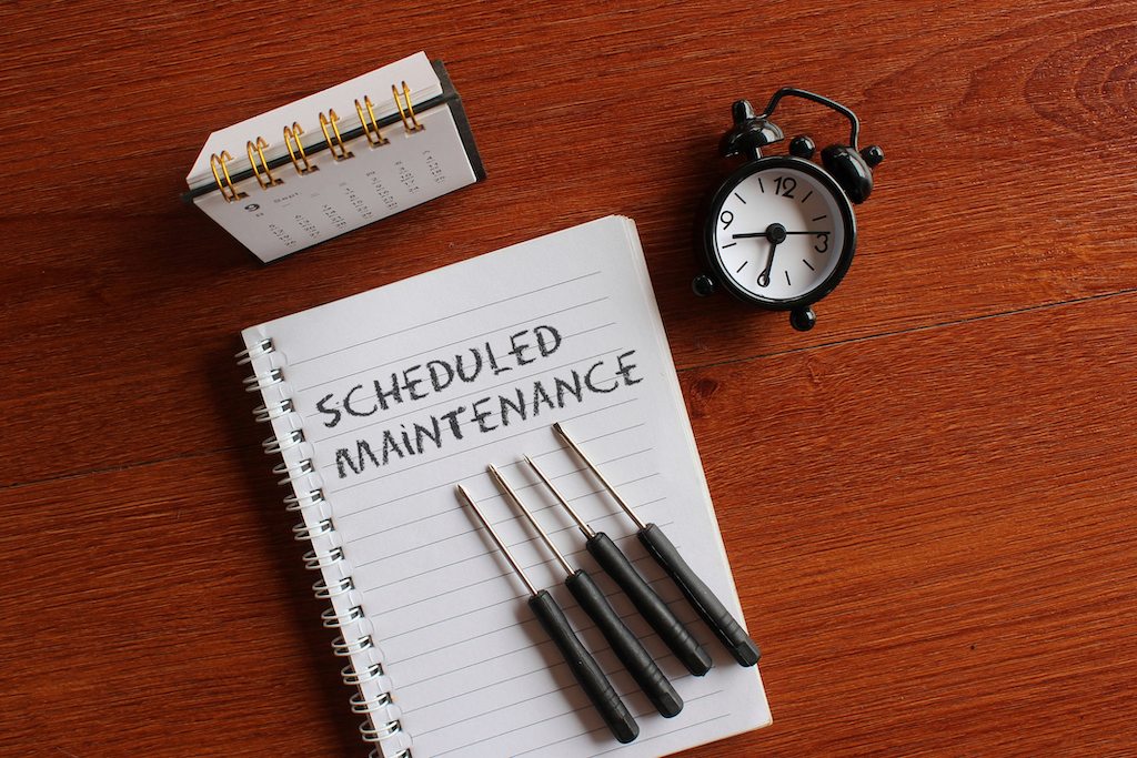 Notebook with tools and 'scheduled maintenance' written on it surrounded by a clock and a calendar. Emergency electrical services.