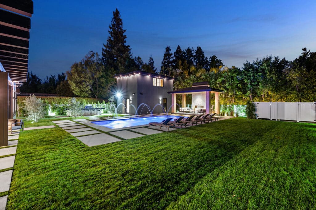 Modern backyard with illuminated swimming pool and patio area, pool bonding keeps swimmers safer in Florence.